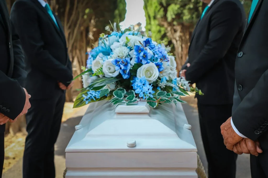 Cercueil blanc orné d'un bouquet de fleurs bleues et blanches entouré de porteurs funéraires